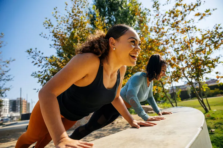 two women working out outdoors having fun and smiling