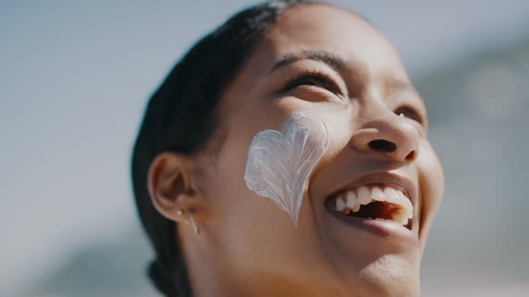 Woman with sunscreen on face to protect skin from sun at beach in summer, laughing on vacation and looking relaxed outside in nature. Closeup portrait of face of a happy person with smile at the sea